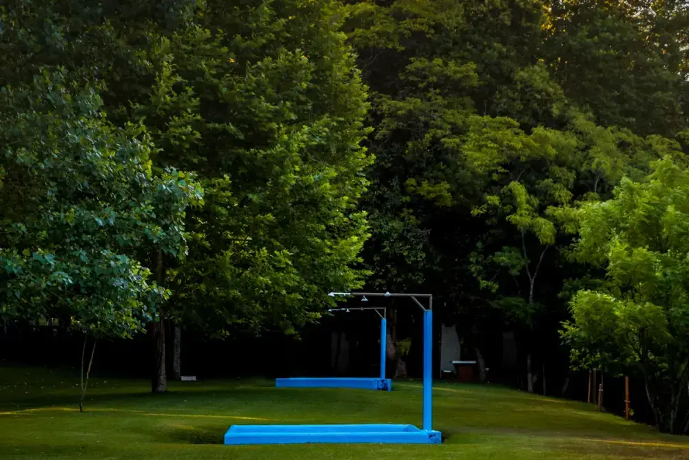 Duas piscinas infantis rasas, azuis, no gramado à sombra das árvores