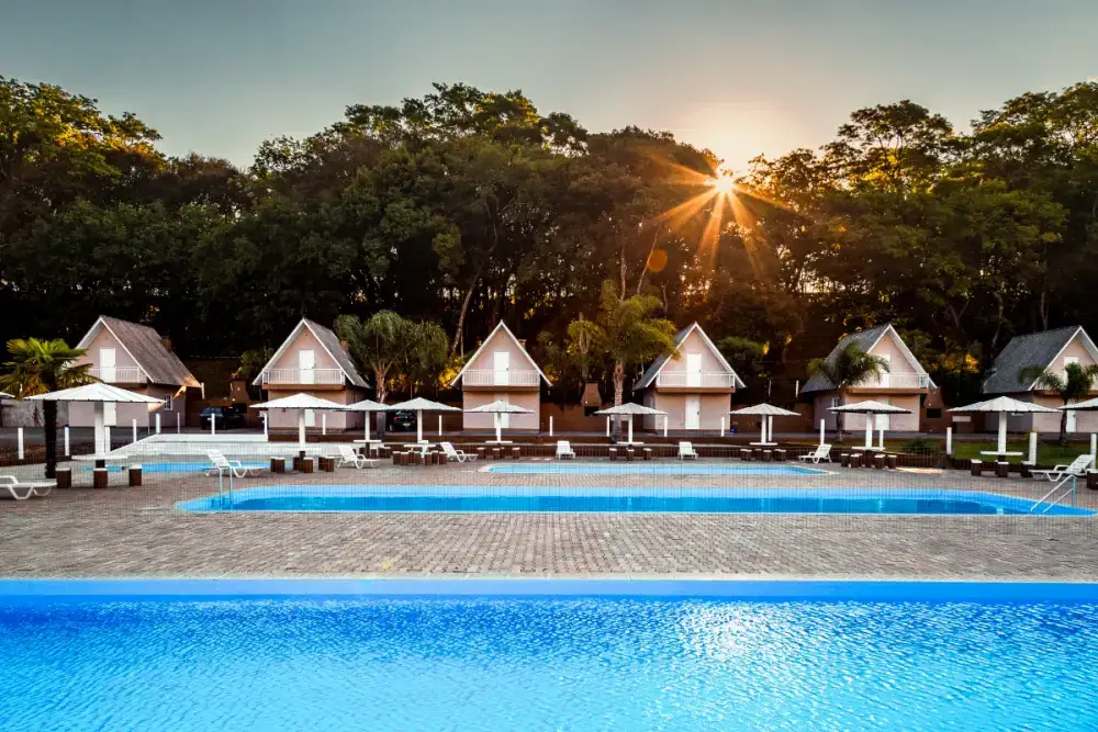 Fileira de cabanas em estilo chalé ao pôr do sol, atrás da piscina