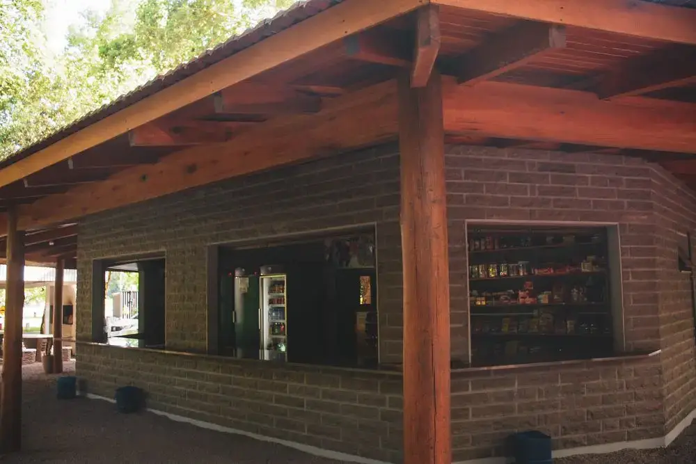 Balcão do bar sob telhado de madeira, com prateleiras de bebidas