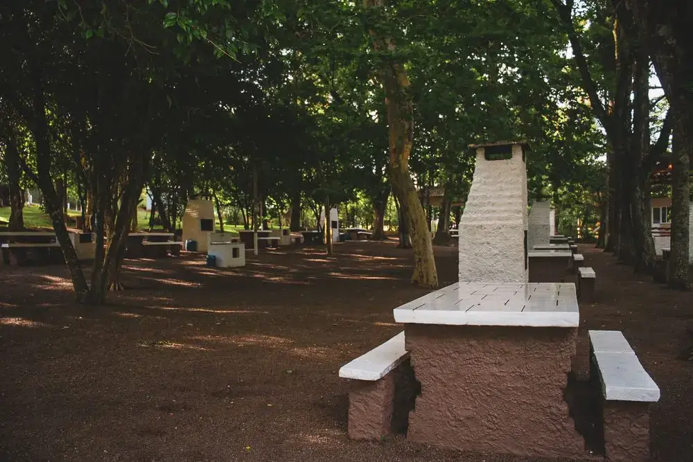 Churrasqueira de alvenaria com mesa e bancos, no bosque à sombra