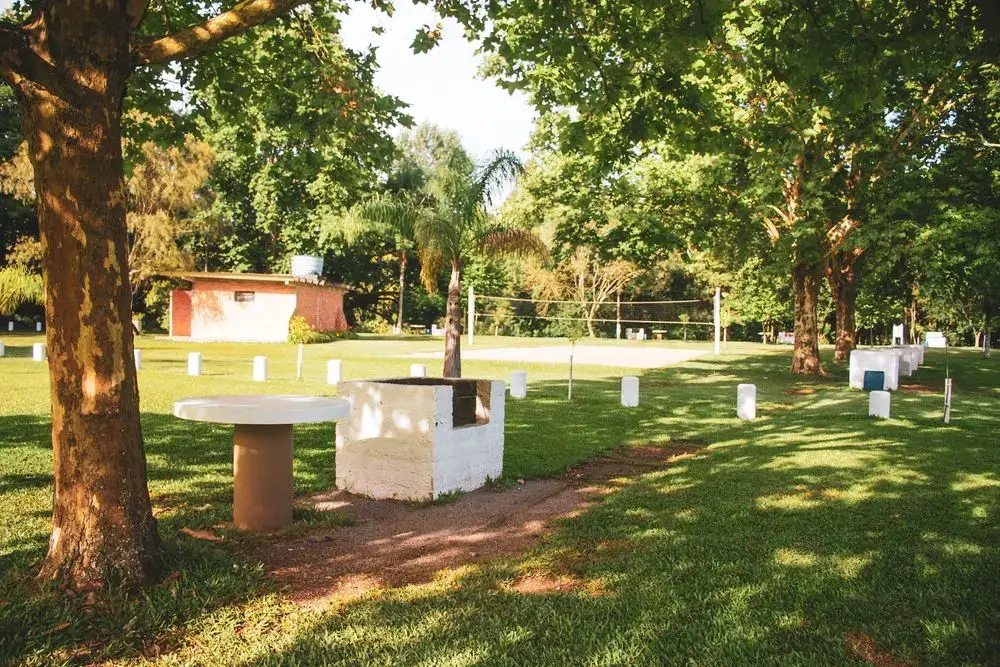 Churrasqueira com mesa redonda no gramado, à sombra das árvores