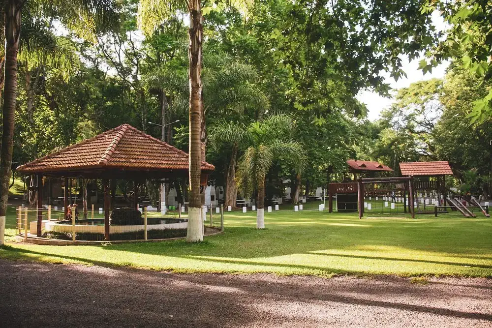 Gazebo de telhado de telha e parquinho ao fundo, no gramado