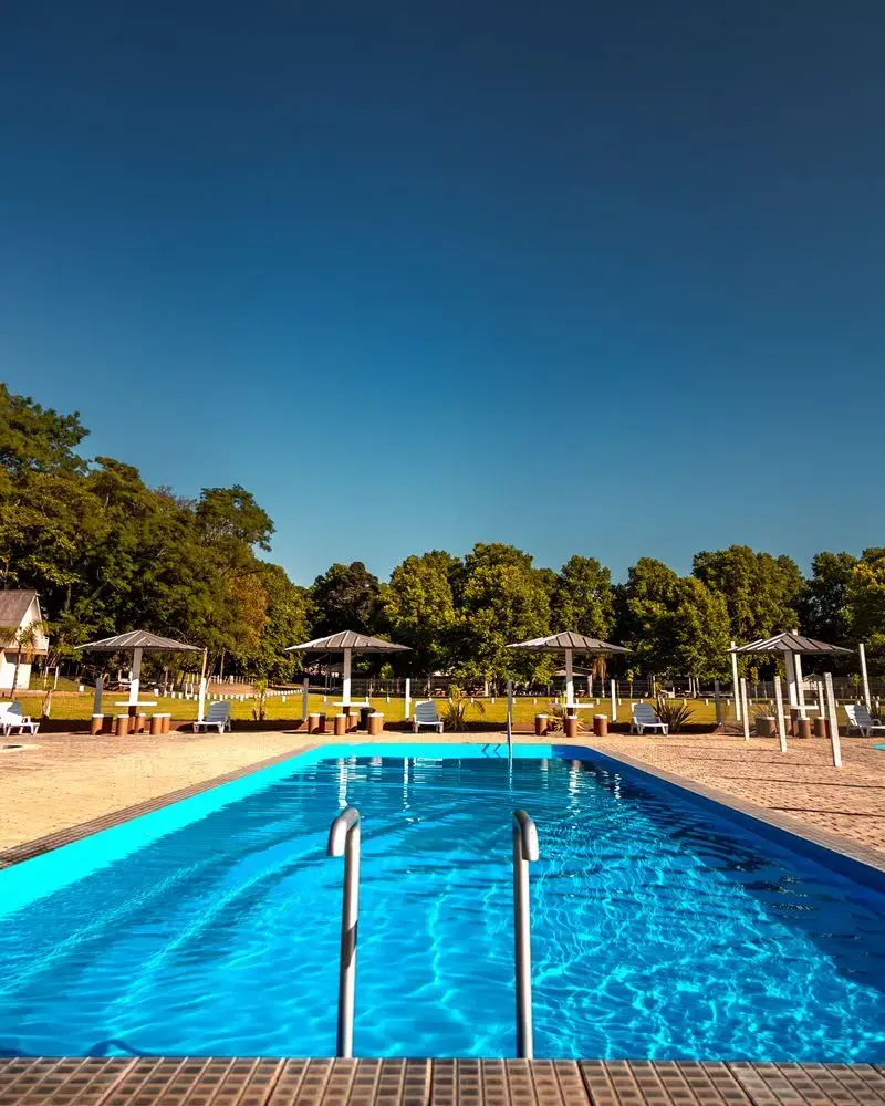 Piscina adulto com escada de inox e guarda-sóis ao fundo